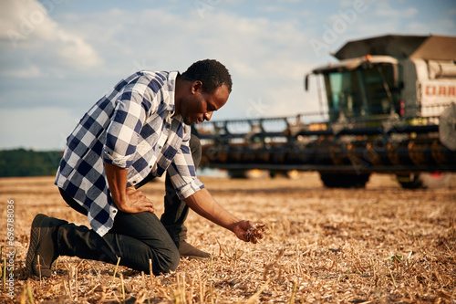 Machinery behind. Beautiful African American man is in the agricultural field