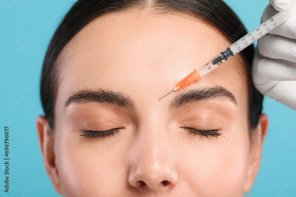 Doctor giving facial injection to young woman on light blue background, closeup. Cosmetic surgery Doctor giving facial injection to young woman on light blue background, closeup. Cosmetic surgery