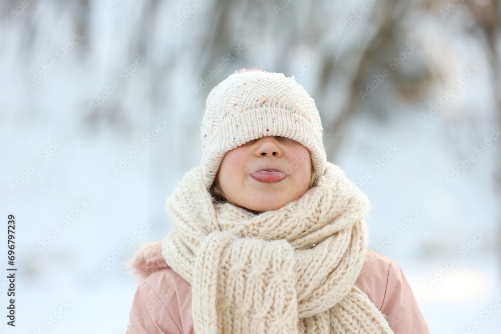 Cute little girl showing her tongue in snowy park on winter day Cute little girl showing her tongue in snowy park on winter day