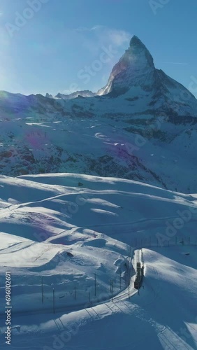 Matterhorn Mountain and Train in Sunny Winter Day. Swiss Alps. Switzerland. Aerial View. Reveal Shot. Drone Flies Forward, Camera Tilts Up. Vertical Video photo