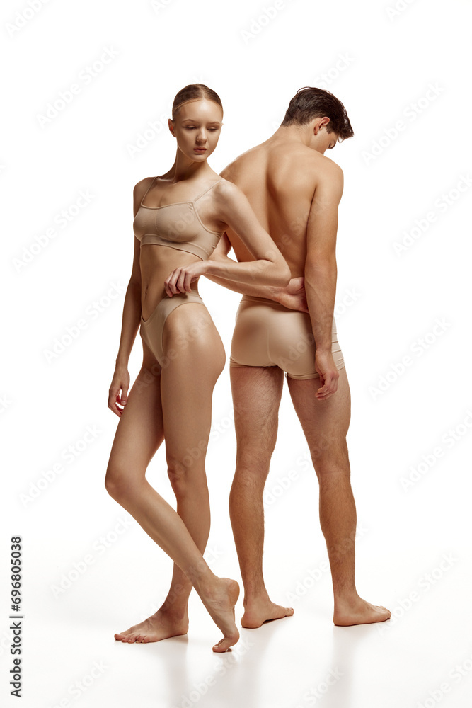 Fototapeta premium Body size portrait of naked couple, woman and man with perfect body shapes posing in beige underwear against white studio background. Concept of beauty, love, body care, cosmetic products, fashion.