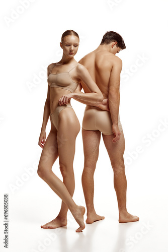 Body size portrait of naked couple, woman and man with perfect body shapes posing in beige underwear against white studio background. Concept of beauty, love, body care, cosmetic products, fashion.