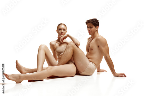 Attractive young man and woman sitting on floor and posing in flesh color lingerie against white studio background. Concept of natural beauty people, love, body care, cosmetic products, fashion.