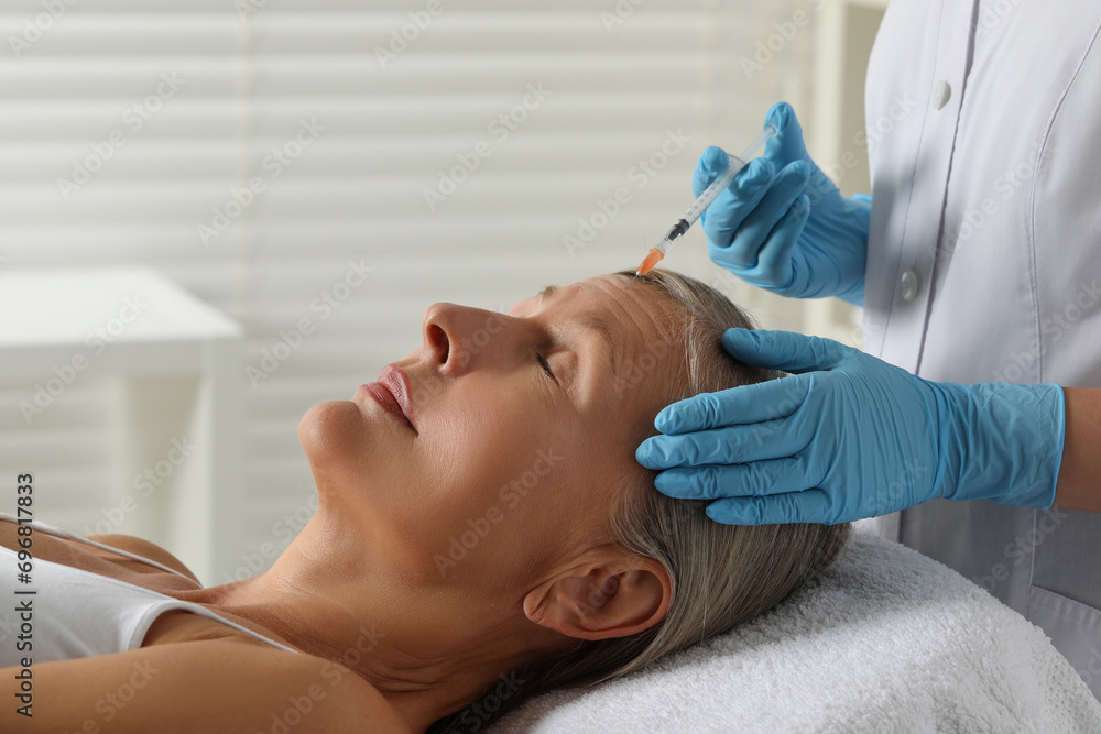 Doctor giving facial injection to senior woman in clinic. Cosmetic surgery