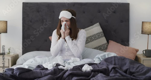 Sick, sneezing and woman blowing nose in bed a with tissue, allergies or viral infection at home. Flu, cough and female person in a bedroom with toilet paper, bacteria or tuberculosis risk in a house photo