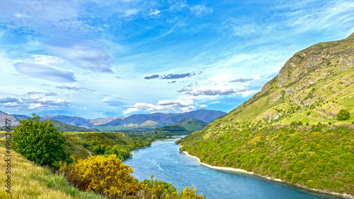River in between mountains summer day New Zealand - blue sky with slights clouds - green mountains traversed by a river on beautiful sky