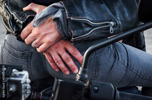 hands of a biker man hugging a biker woman's back sitting on a motorcycle