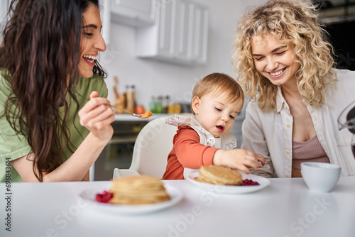 merry beautiful lgbt couple having delicious breakfast with their baby girl, family concept