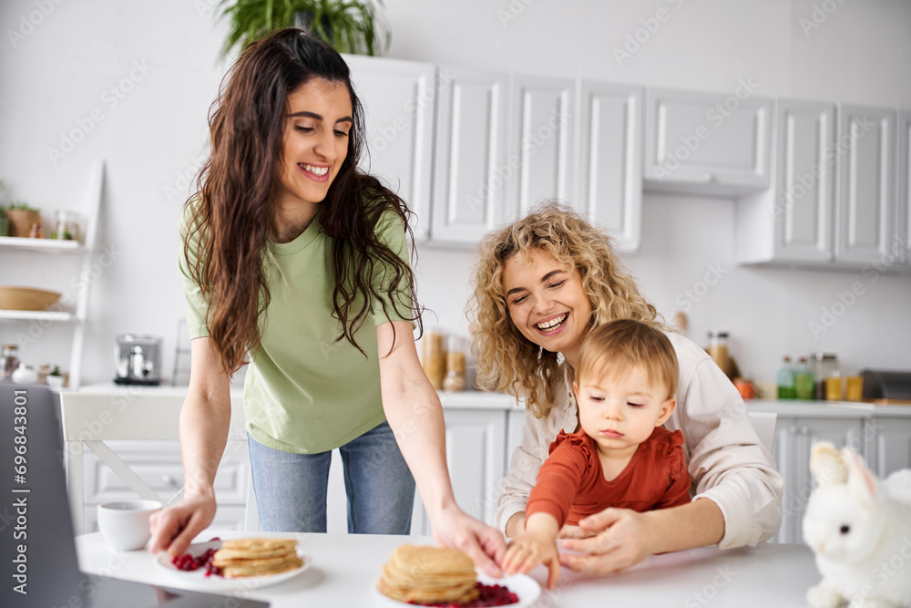 attractive joyous lesbian couple having pancakes on breakfast with their baby girl, family concept attractive joyous lesbian couple having pancakes on breakfast with their baby girl, family concept