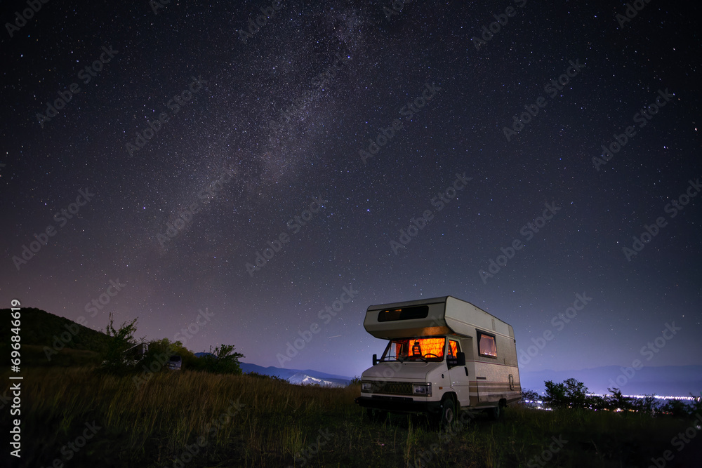 Motorhome, camper, at night under the starry sky next to a tree on a hill - obrazy, fototapety, plakaty 