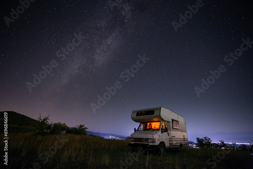 Motorhome, camper, at night under the starry sky next to a tree on a hill