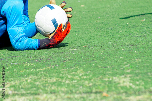 Young goalkeeper grabbing soccer ball and defending his team's goal