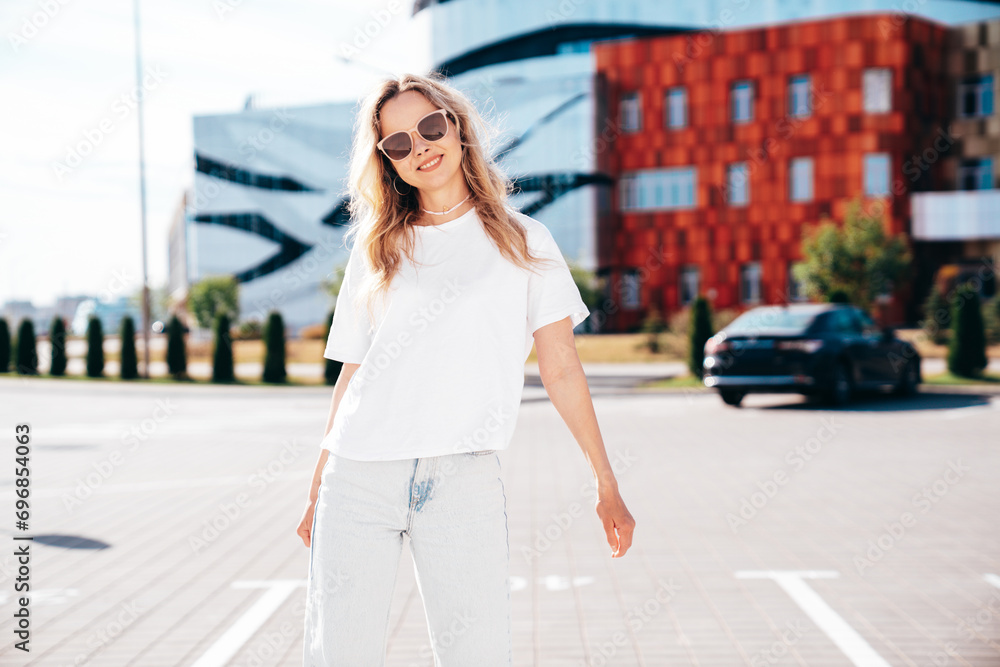 Portrait of beautiful smiling model in sunglasses. Female dressed in summer hipster white T-shirt and jeans. Posing near wall in the street. Funny and positive woman having fun outdoors Portrait of beautiful smiling model in sunglasses. Female dressed in summer hipster white T-shirt and jeans. Posing near wall in the street. Funny and positive woman having fun outdoors
