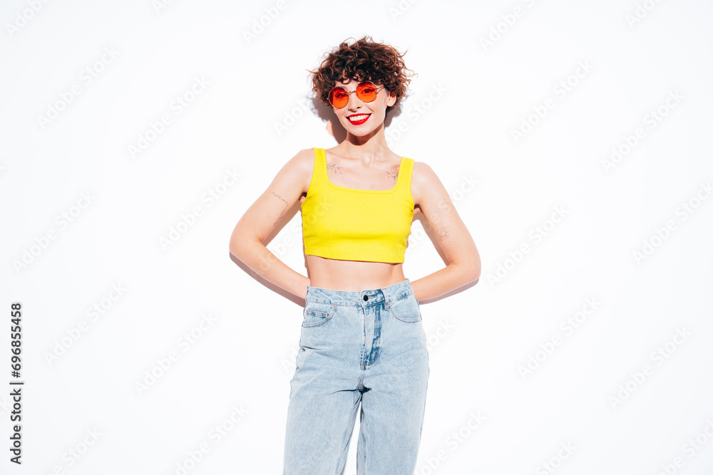 Young beautiful smiling female in trendy summer yellow tank top. Carefree woman posing near white wall in studio with curly hairstyle. Positive model having fun, going crazy. Cheerful and happy Young beautiful smiling female in trendy summer yellow tank top. Carefree woman posing near white wall in studio with curly hairstyle. Positive model having fun, going crazy. Cheerful and happy