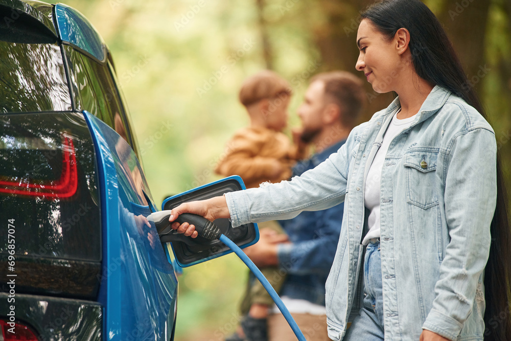 Obraz premium Conception of wellness. Mother, father and little son are waiting for electric car to charge outdoors