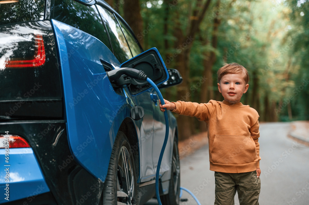Cute young boy is charging the blue electric car outdoors Cute young boy is charging the blue electric car outdoors