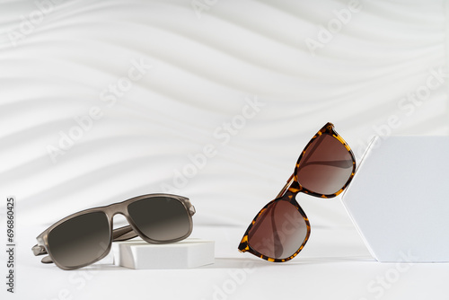 Men's and women's Trendy sunglasses on podiums on a white background. Fashionable eyewear collection. Minimalism. Sunglasses promotion. Eyewear fashion. Optic store discount banner, sale. Copy space