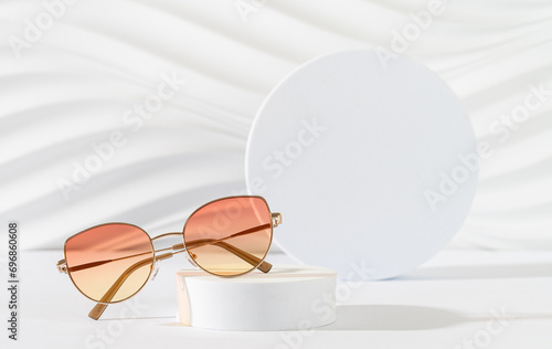 Woman's sunglasses with color lenses in metallic frame on a podium on a white background. Trendy sunglasses still life, minimal style. Optic store discount banner, sale, promotion. Copy space