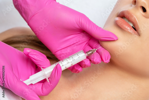 Cosmetologist does injections for lips augmentation and anti wrinkle in the nasolabial folds of a beautiful woman. Women's cosmetology in the beauty salon. photo