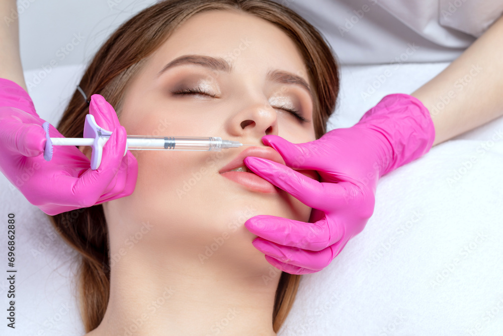 Cosmetologist does injections for lips augmentation of a beautiful woman. Women's cosmetology in the beauty salon.