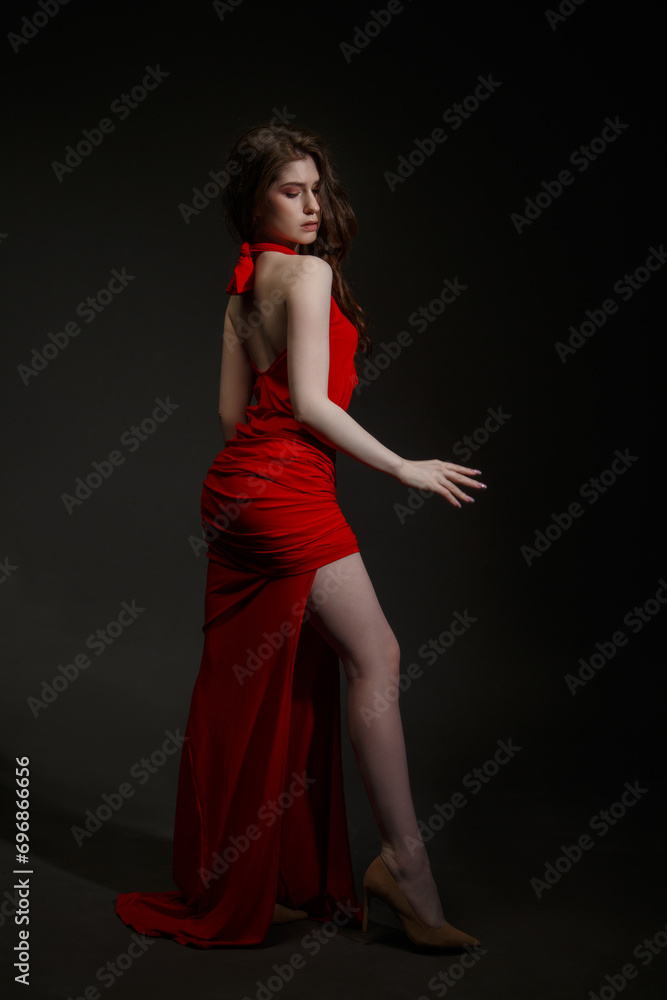 Slender girl in a long red dress on a black background.