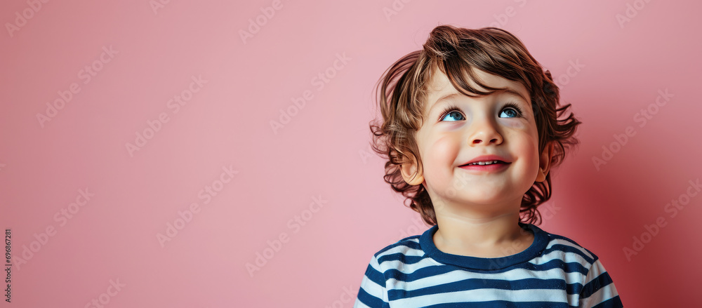 Portrait of pretty brunette hair little boy child with expression of joy on face, cute smiling isolated on a flat pastel pink background with copy space. Template for banner, text place.