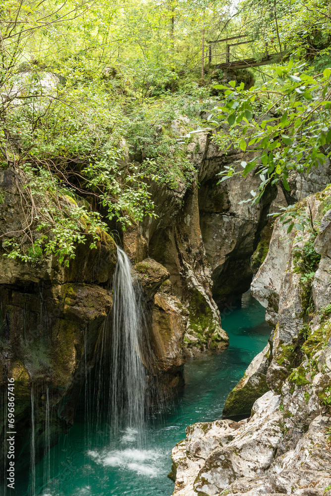 Landscape of Slovenia. A small waterfall flows into the turquoise waters of the Soča River at the bottom of a narrow canyon Landscape of Slovenia. A small waterfall flows into the turquoise waters of the Soča River at the bottom of a narrow canyon