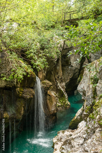 Landscape of Slovenia. A small waterfall flows into the turquoise waters of the Soča River at the bottom of a narrow canyon