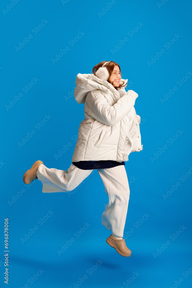 Full length portrait of cheerful, happy girl dressed warm, winter outfit to shop because began sale season against blue background. Concept of New Year, Christmas, winter holidays, shopping. Full length portrait of cheerful, happy girl dressed warm, winter outfit to shop because began sale season against blue background. Concept of New Year, Christmas, winter holidays, shopping.