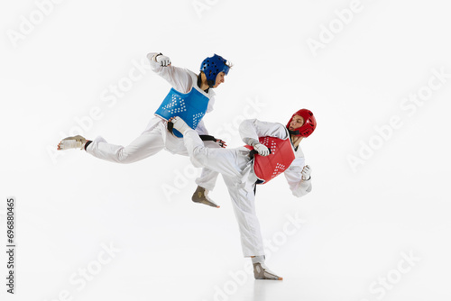 Competitive strong young men, taekwondo, karate athletes in motion, fighting, training isolated over white background. Concept of martial arts, combat sport, competition, action, strength, education