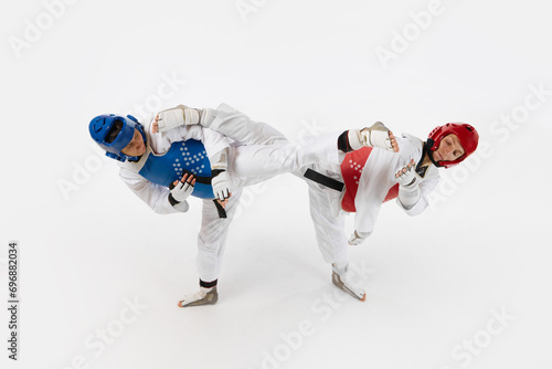 Competitive young men, taekwondo athletes fighting, hitting with legs isolated over white background. Concept of martial arts, combat sport, competition, action, strength, education
