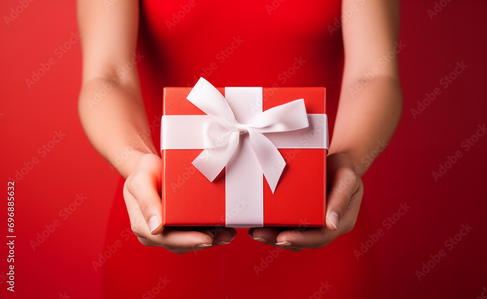 Woman's hands holding a red gift box with a white bow over red pastel background Woman's hands holding a red gift box with a white bow over red pastel background