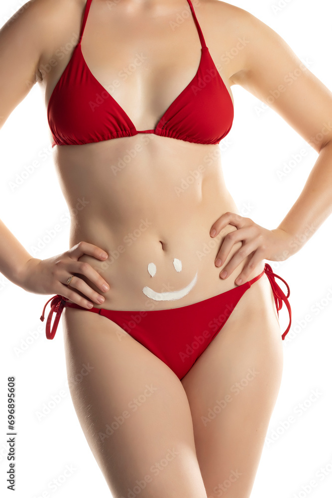 Young woman in red bikini with cosmetic product in smile shape on her belly on white background. Young woman in red bikini with cosmetic product in smile shape on her belly on white background.