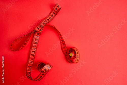 Red measuring tape on a red background. Tool for measuring length and volume. Tape for measuring in the clothing industry or the volume of the human body