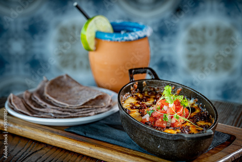 Queso Fundido. Oaxaca and chihuahua cheese on a skillet with chorizo and pico de gallo, served with blue corn tortillas