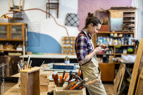 Portrait of young female carpenter using mobile phone in her workshop photo