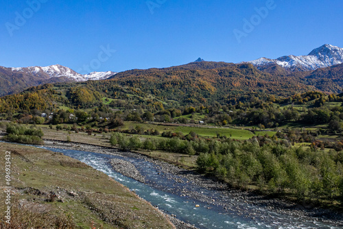 A serene landscape showcasing a meandering river with autumn-colored forests and snow-capped mountains, exemplifying rural beauty and the change of seasons