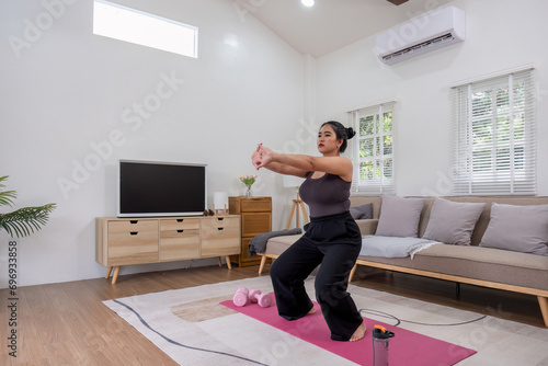 Fat Asian woman stretching at home on a fitness mat. Practicing activities at home online exercise classes Practice stretching on your yoga mat at home to stay healthy and in shape.