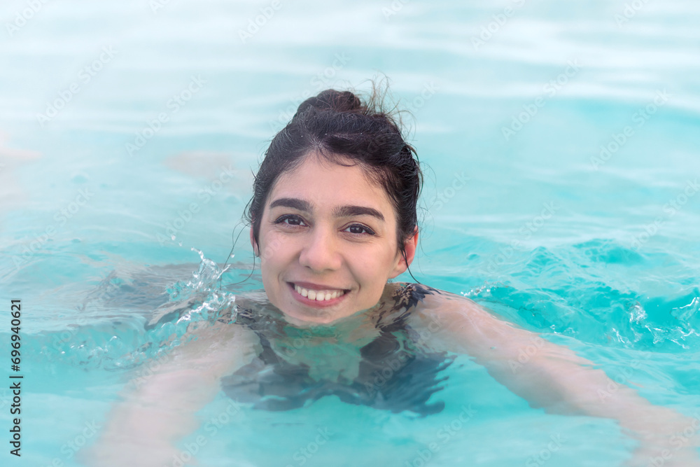 A smiling young dark-haired woman bathes in a hot thermal spring on a winter day.Self-care,healthy lifestyle,leisure activity,mental health concept.