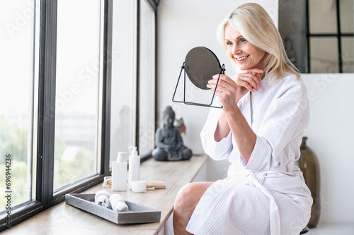 Smiling mature woman looking at mirror and enjoy her healthy soft face skin photo