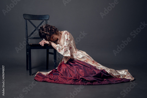 Young beautiful sad crying woman in medieval style dress sitting on the floor near chair
