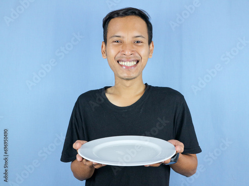 A young Asian man in a black t-shirt stands and holds an empty plate showing the dish. photo