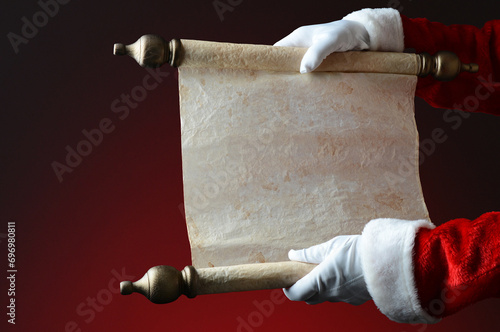 Santa Claus holding naughty and nice scroll over a light to dark red background. The scroll is blank wit copy space. Closeup only showing santas hands and arms. photo