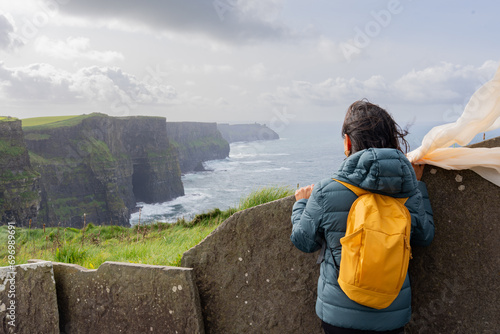 Woman on her back with backpack enjoying a splendid view from the top of the Mother's cliff in Ireland photo