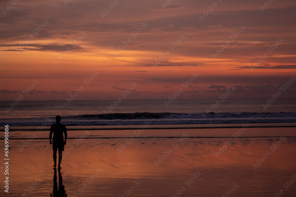 A person silhouetted against a vibrant sunset on the beach