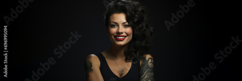Front view. Female portrait. Horizontal banner. Beautiful young tattooed brunette Hispanic woman with curly hair looks at the camera with a smile isolated on a black background. Copyspace