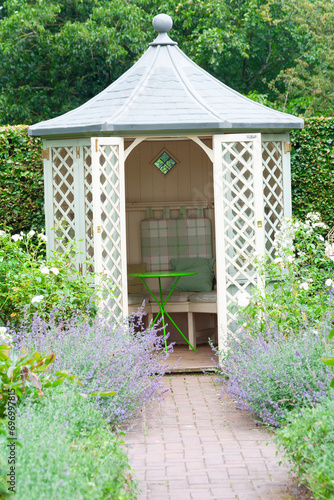 Canvas Print Summer time and the living is easy- white trellis wooden summerhouse in domestic garden set up with table and chair in it ready for summer outdoor meals