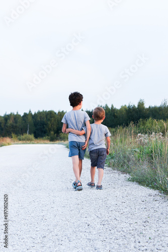 Two boys, two brothers or two friends, are walking along the road hugging and talking. The picture was taken from the back. High quality photo
