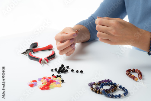 Jewelry making. Making a bracelet of colorful beads. Female hands with a tool on a white background. Selective focus.