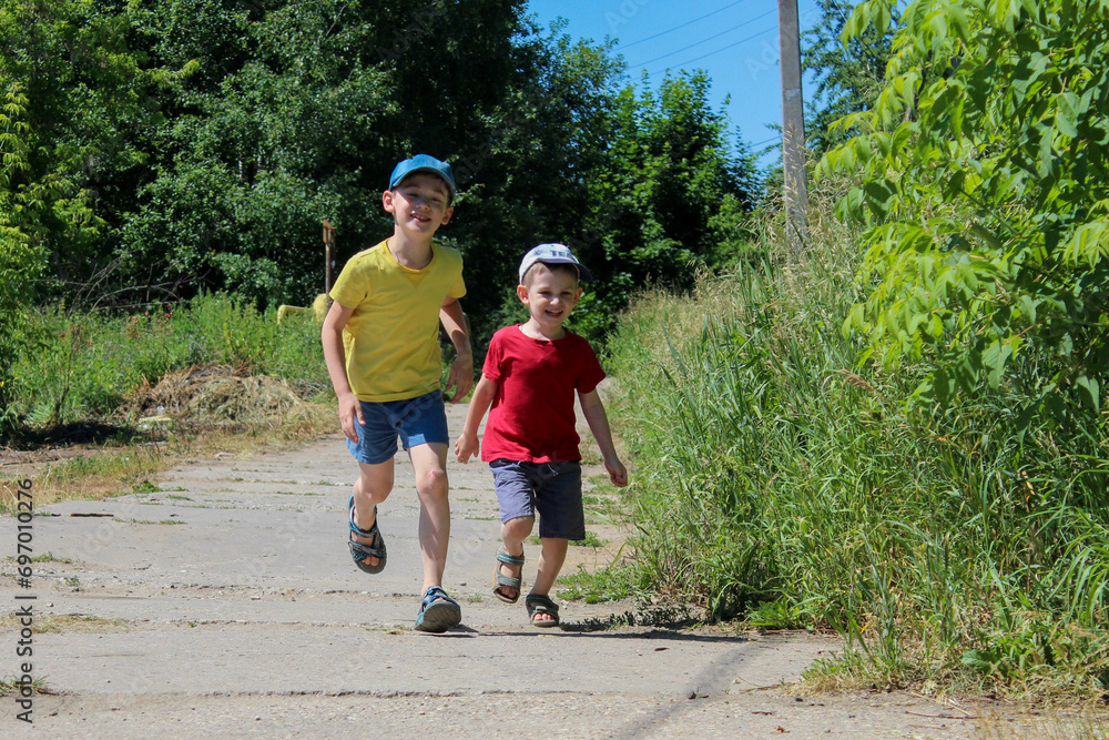 Two cheerful boys, brother or friend are running forward in bright clothes, red and yellow T-shirts, caps on their heads. High quality photo Two cheerful boys, brother or friend are running forward in bright clothes, red and yellow T-shirts, caps on their heads. High quality photo